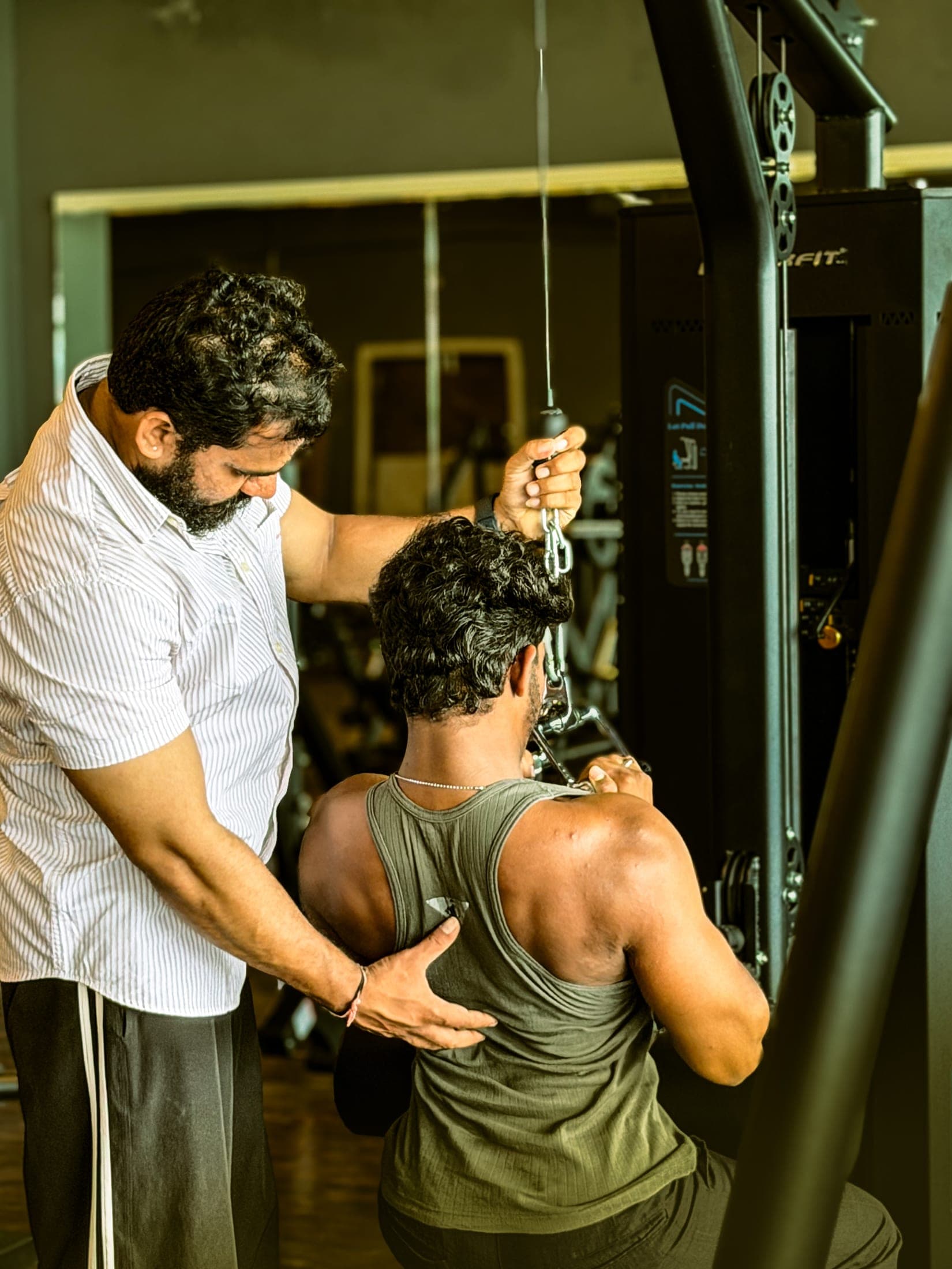 Trainer coaching a member on the cable machine across the spacious Golds's Gym Gajwel training floor