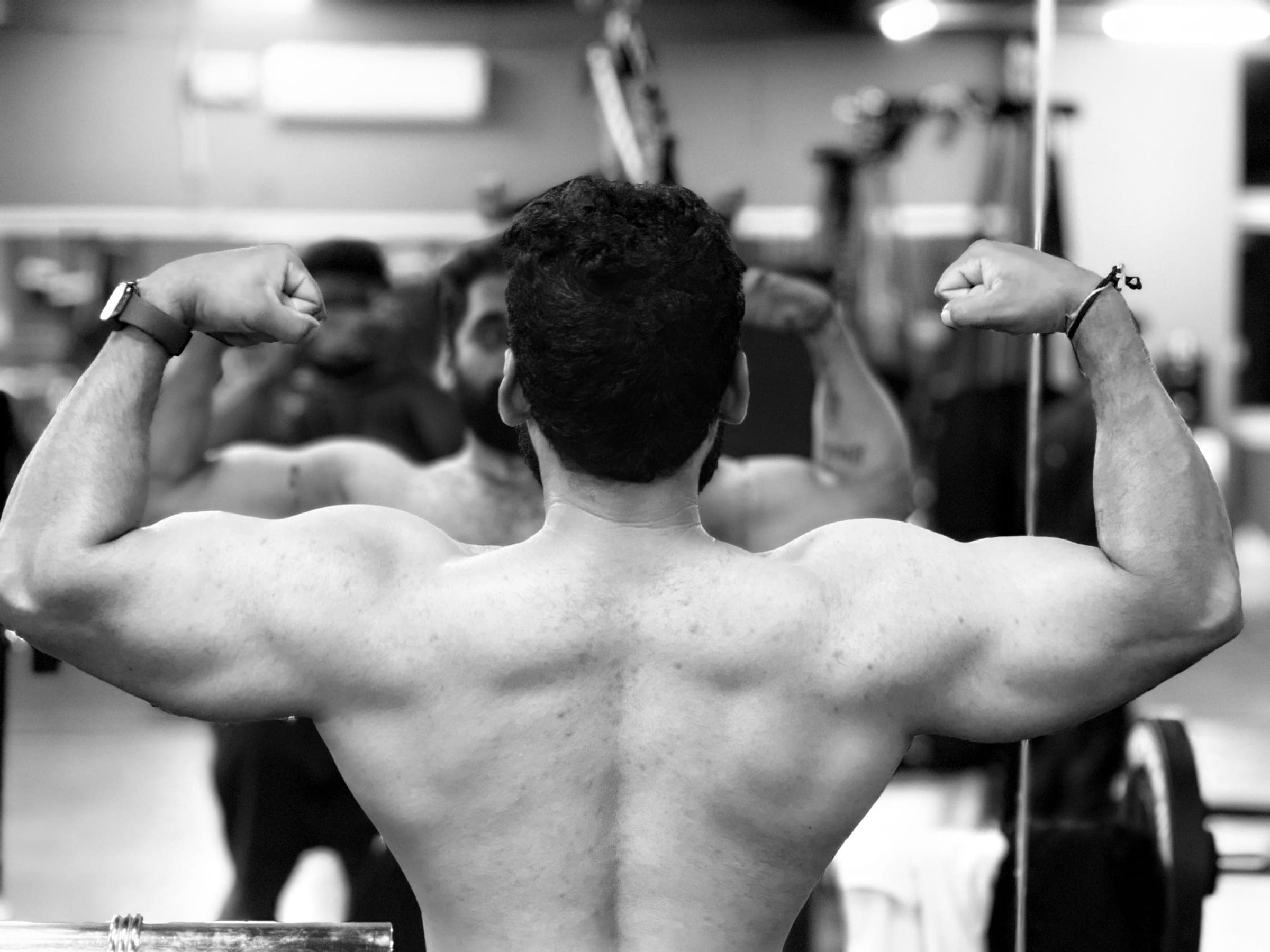 Member flexing a muscular back double-biceps pose in the gym mirror