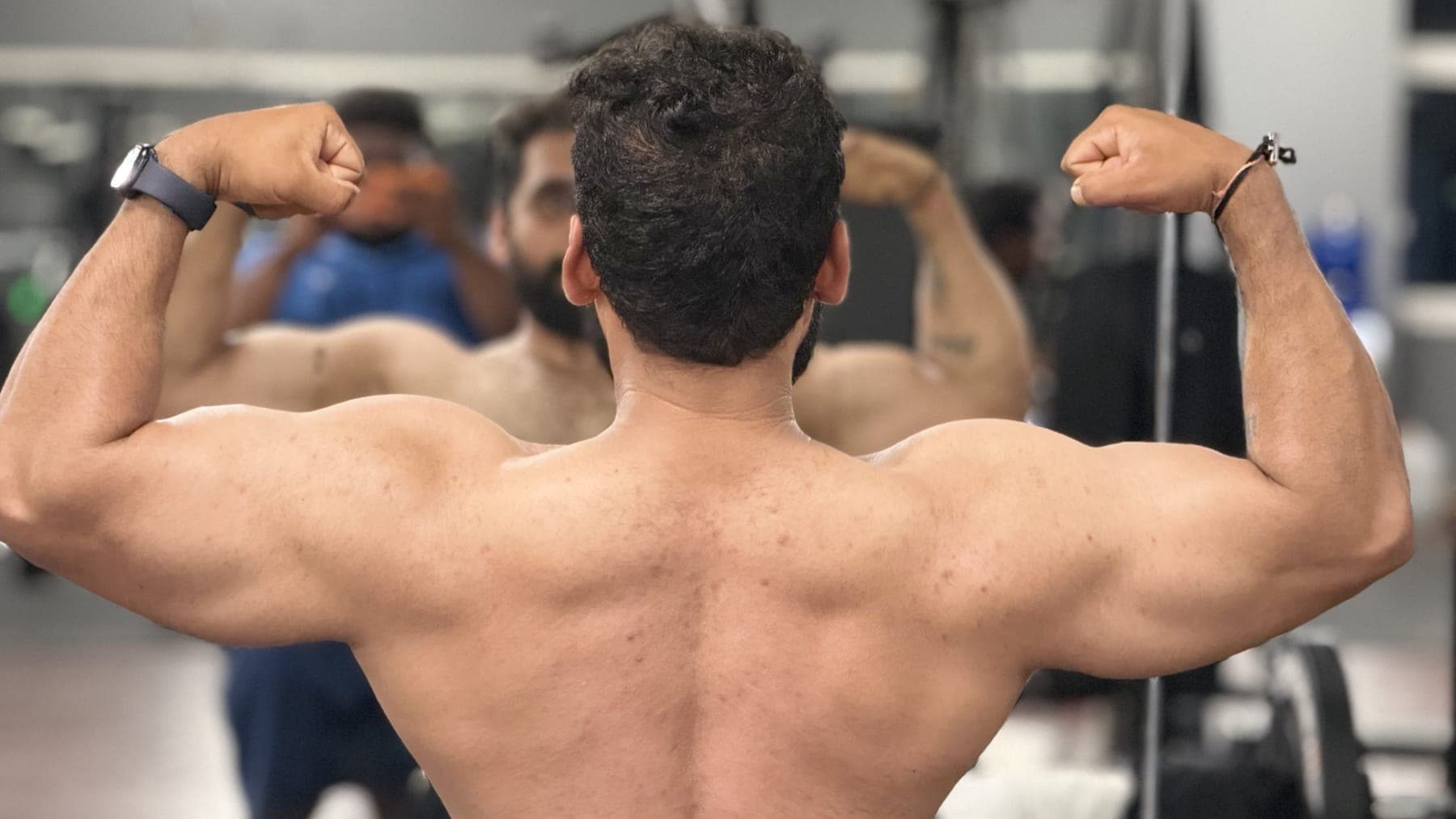 Member flexing a back double-biceps pose in the gym mirror