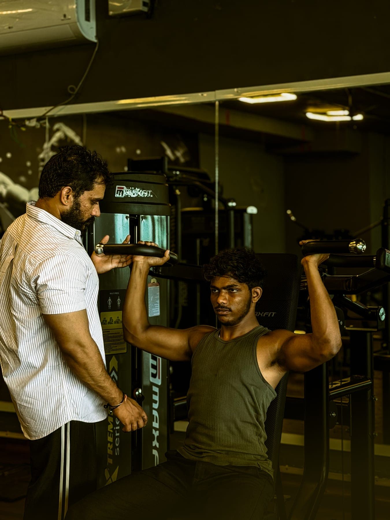 Trainer guiding a member on the shoulder press machine
