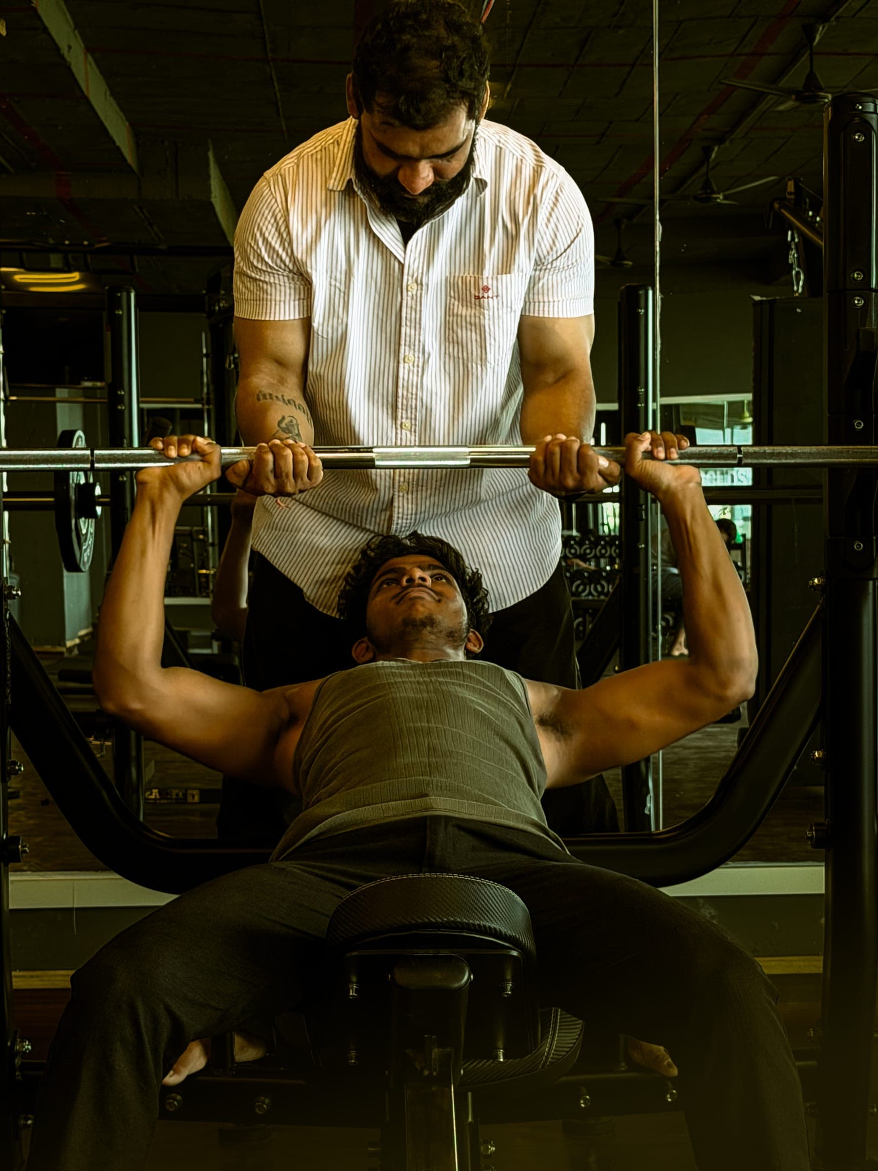 Trainer spotting a member during a heavy barbell bench press at Golds's Gym Gajwel