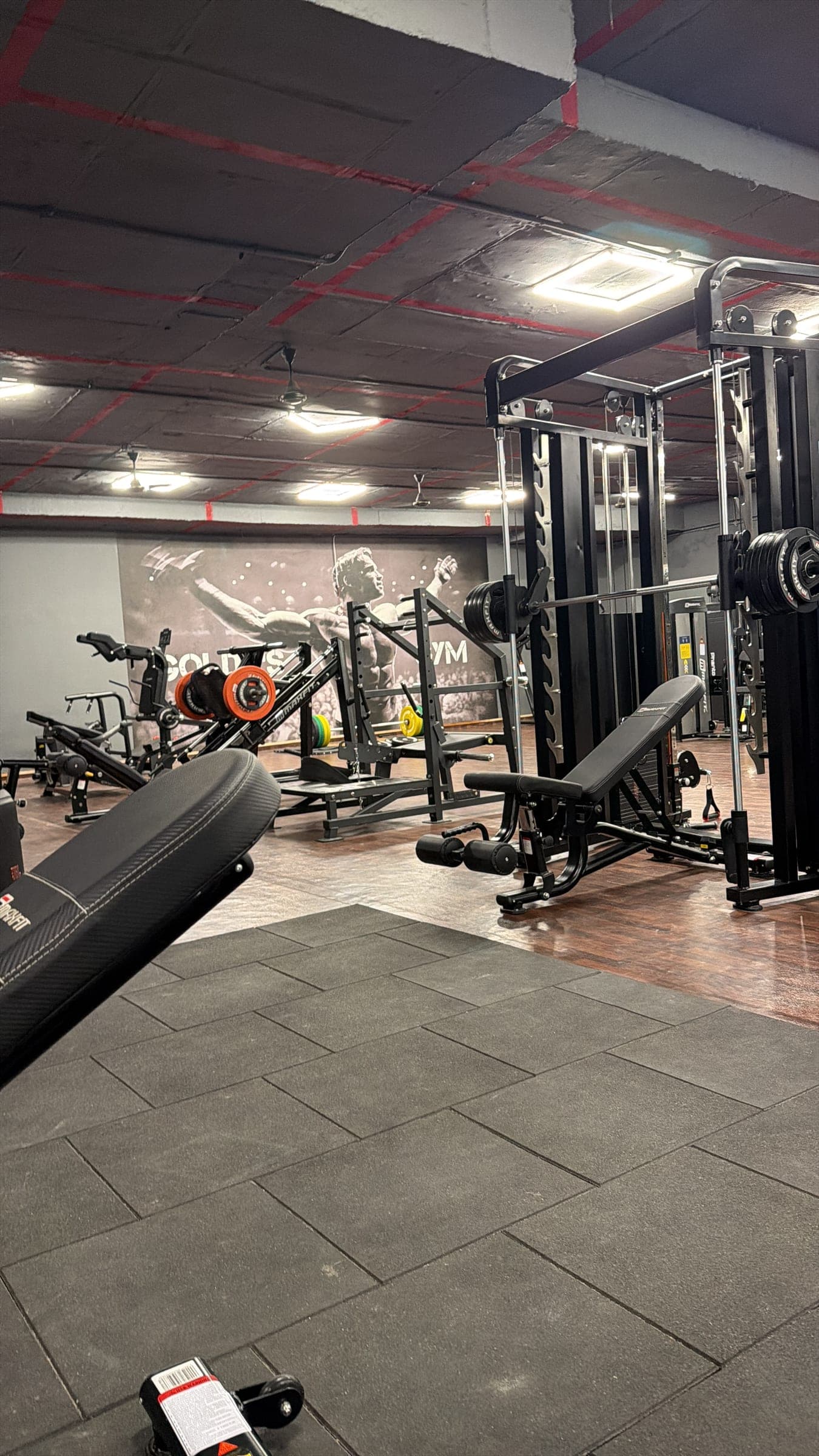 Wide view of the Golds's Gym Gajwel training floor, lined with strength equipment beneath the gym's signature mural