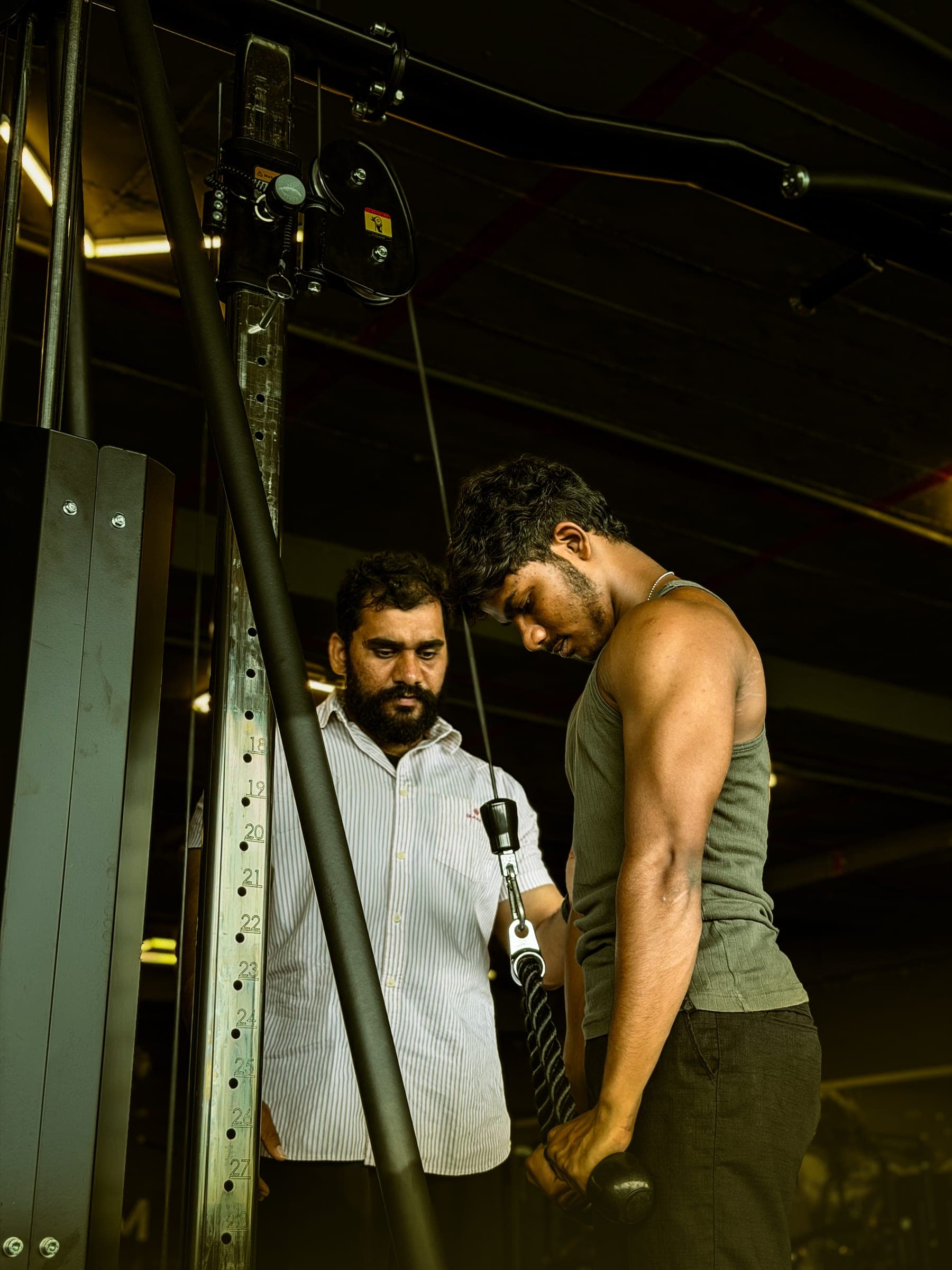 Trainer guiding a member through a cable pull exercise under dramatic gym lighting